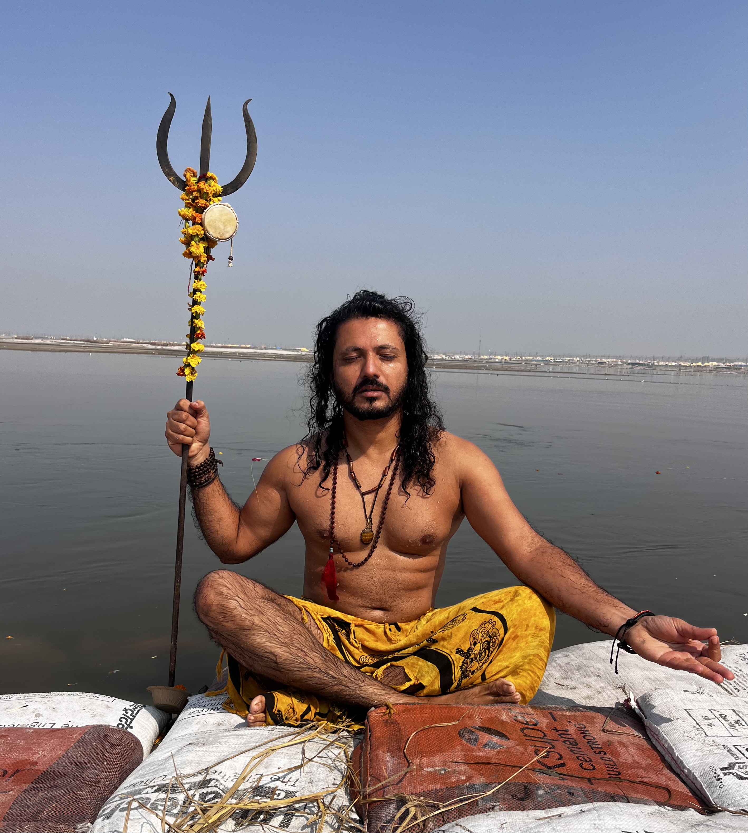 Yogi Rohan seated in meditation with a trident near sacred water